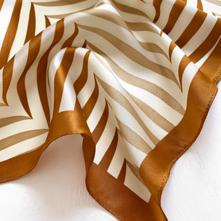 Luxurious silk bandana with elegant golden caramel and cream striped pattern, featuring a shimmering finish and hemmed border, draped to showcase texture