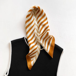Golden caramel and cream striped silk bandana scarf with geometric pattern, elegantly draped on black garment against white background