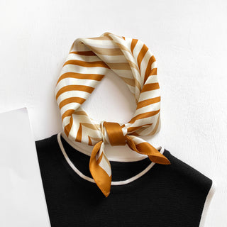 Golden caramel striped silk bandana tied at neck of black top, showing luxurious sheen and geometric pattern with cream and burnt orange tones
