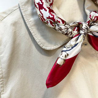 Silk bandana scarf with red and white pattern featuring decorative gold rings and cartoon bear motif, tied stylishly on beige garment collar.