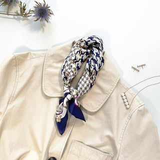 Indigo blue silk scarf with houndstooth pattern styled on beige jacket collar, accessorized with pearl jewelry and dried flowers in background