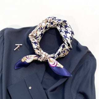 Indigo blue houndstooth silk scarf tied stylishly on navy blazer with decorative gold chain pattern and purple edge details