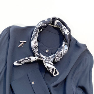 Black silk bandana scarf with white fern pattern tied around navy blouse collar, accessorized with pearl pin on shoulder