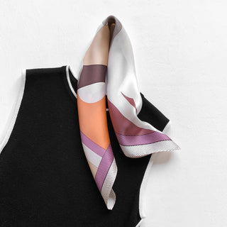 Pink silk bandana scarf with geometric patterns in mauve, peach, and white, elegantly draped on black garment with white trim