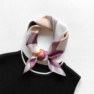 Pink silk bandana scarf with geometric pattern in purple, peach and white tones tied elegantly around black sweater collar