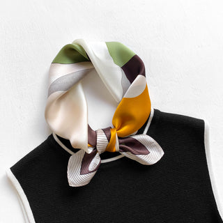 Silk bandana scarf in geometric pattern featuring olive green, cream, mustard yellow and burgundy blocks, elegantly knotted on black garment