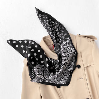 Black silk bandana scarf with white paisley and polka dot patterns elegantly draped through the collar of a beige coat