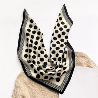 Silk bandana scarf with cream background, black polka dots and striped border, elegantly draped on beige knit fabric
