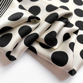 Luxurious silk bandana scarf with black polka dots on cream background, showing shiny fabric texture with black striped border edge