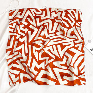 Luxurious square silk bandana with burnt orange geometric zigzag pattern on cream background, showing the scarf's smooth texture and vibrant design