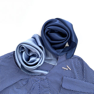 Two silk scarves elegantly arranged - one navy blue and one sky blue - displaying their luxurious sheen atop a textured blue fabric background