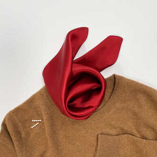 Burgundy silk scarf elegantly draped around collar of camel-colored sweater, showcasing its lustrous sheen and smooth texture.