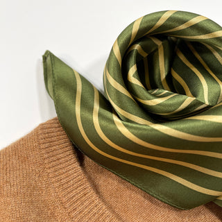 Moss green silk scarf with gold diagonal stripes elegantly draped on light brown knit fabric, showcasing its lustrous texture and pattern