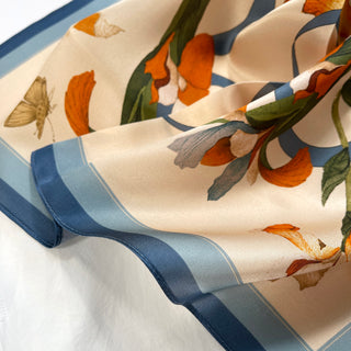 Silky cream bandana with blue border, featuring orange iris flowers, green leaves, and delicate butterfly pattern in elegant silk fabric