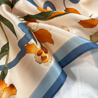 Luxurious Iris Melody silk scarf with blue border and orange iris flowers on cream background, showing soft fabric folds and sheen