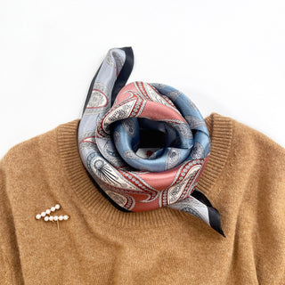 Silk paisley scarf in salmon pink and light blue with black border, styled as a neckerchief on camel sweater with pearl brooch
