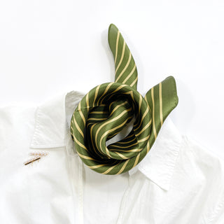 Moss green silk bandana with diagonal gold stripes elegantly twisted on a white shirt, showcasing its shiny texture and versatile styling.