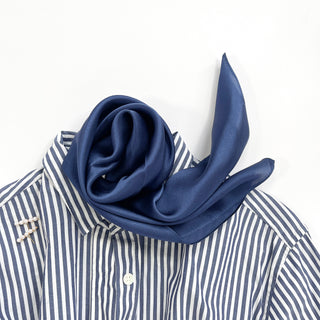 Navy blue silk scarf elegantly draped on a blue and white striped shirt collar, showcasing its luxurious sheen and smooth texture.