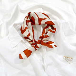 Silk bandana scarf with burnt orange zigzag pattern on cream white background, styled with white shirt and pearl pin accessory