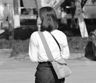 Black and white image of person wearing stylish small messenger bag crossbody with white shirt and jeans, showing the bag's compact design