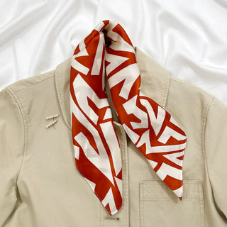 Luxurious burnt orange zigzag pattern silk bandana scarf displayed on a beige blazer, showcasing its smooth texture and elegant design