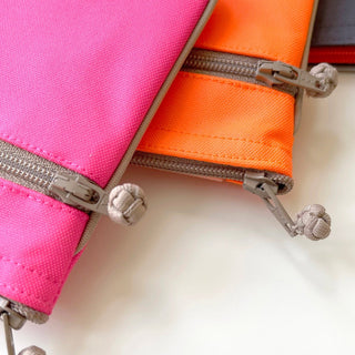 Close-up of recycled double zipper wallets in vibrant neon pink and orange, showing quality YKK zippers with fabric pulls and piped edge detailing