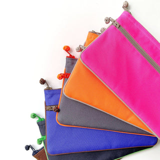 Recycled double zipper wallets arranged in a fan display showing vibrant colors: neon pink, orange, blue, gray, and black with contrasting piping and zipper pulls.