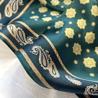 Close-up of luxurious teal silk neckerchief featuring gold paisley border pattern and decorative octagonal star motifs in yellow and white.