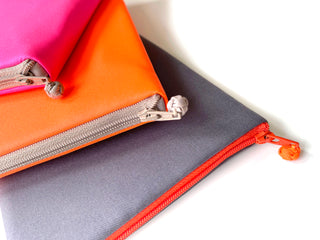 Colorful recycled Kindle cases in bright pink, orange, and navy blue with quality YKK zippers, showcasing the multi-functional travel organizer design