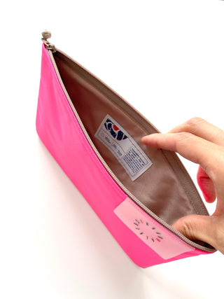 Bright neon pink recycled waterproof iPad case with beige interior lining, showing YKK zipper and product label, held open to display inner pocket