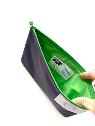 Open recycled iPad case with navy exterior and bright green interior lining, featuring Japanese YKK zipper and product label, shown being held open