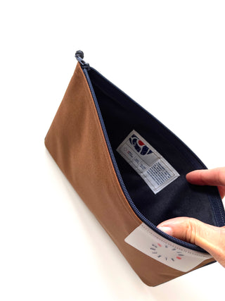 Open brown iPad case with navy blue zipper and lining, showing interior label and brand tag, made from recycled materials, waterproof design