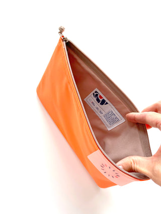Bright neon orange recycled waterproof iPad case shown open, featuring beige interior lining, manufacturer's tag, and YKK zipper closure