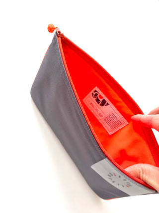 Gray recycled waterproof iPad case with bright neon orange interior lining, YKK zipper, and brand label, shown partially open against white background