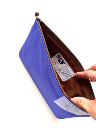 Open bright blue recycled waterproof iPad case with brown interior lining, showing product tag and YKK zipper, held by hand to display interior