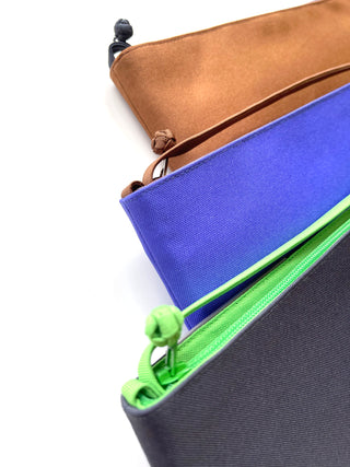 Stacked small crossbody phone wallets in four colors: caramel brown, vibrant blue, lime green, and gray, each with matching zipper pull details