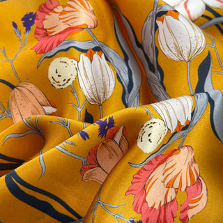 Mustard yellow silk scarf with floral print featuring pink, white, and coral flowers with blue accents, showcasing luxurious fabric texture