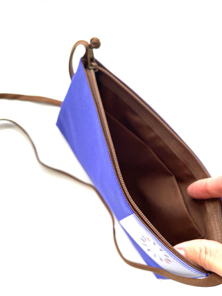 Open bright blue crossbody phone wallet showing brown interior with card sleeves, YKK zipper, and thin shoulder strap, held open to display capacity