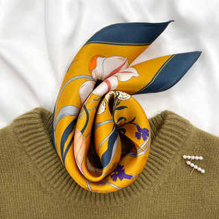 Mustard yellow silk scarf with navy border displayed on olive sweater, featuring floral and butterfly pattern in white, coral and purple hues.