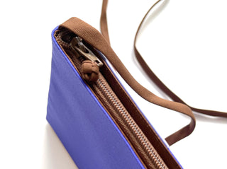Purple crossbody phone wallet with brown trim, YKK zipper, and thin brown shoulder strap, showing partially open interior compartments