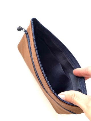 Open recycled double zipper wallet with tan exterior, navy blue interior and trim, showing spacious compartment with hands holding it open