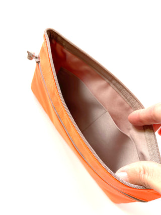 Open neon orange recycled wallet showing interior compartment with light lining and piping detail, held open by two fingers