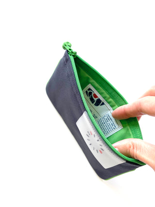 Recycled zipper wallet in navy blue with bright green trim and interior, featuring decorative button detail and product tag, shown open with hands holding it