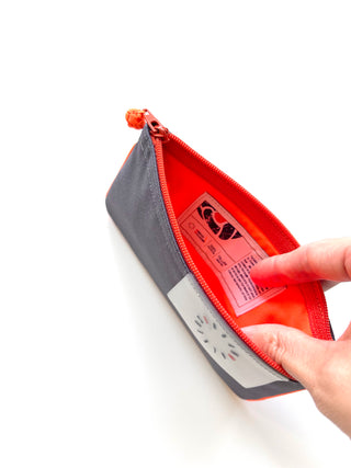 Recycled zipper wallet with gray exterior, bright orange interior, decorative button detail, and piped edges, shown open with product tag visible