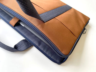 Recycled RPET laptop briefcase in camel brown with navy blue trim, showing zippered compartment with laptop inside and fabric handles