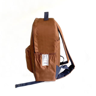Stylish caramel brown RPET waterproof backpack with navy blue straps, side view showing clean piping detail and brand label on exterior pocket