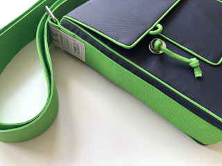 Small messenger bag with navy blue body and bright green trim, featuring adjustable strap, metal hardware, and eco-friendly tag showing recycled materials