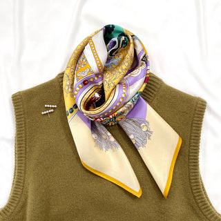 Luxurious silk scarf with yellow and lilac vintage pattern, elegantly draped on olive green sweater, featuring decorative tassels and gold border trim