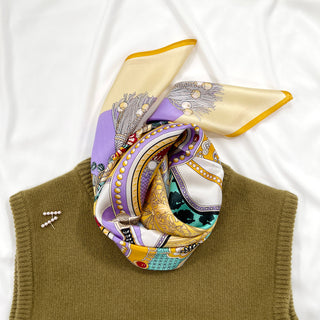 Luxurious yellow and lilac silk scarf with vintage decorative pattern, elegantly folded and styled with an olive green knit garment on white background.