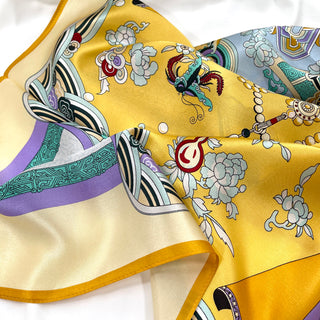 Luxurious yellow silk scarf with ornate floral and bird pattern featuring lilac borders, decorative pearls, and vintage-inspired motifs on shimmering fabric.